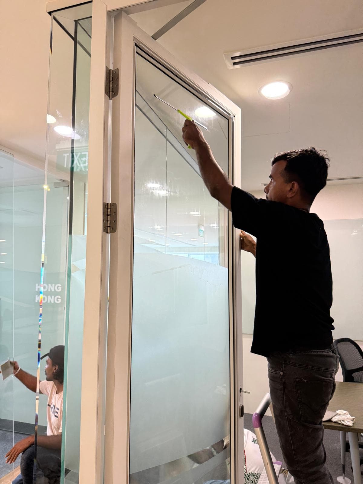 Technician repairing a misaligned glass door in a Singapore office