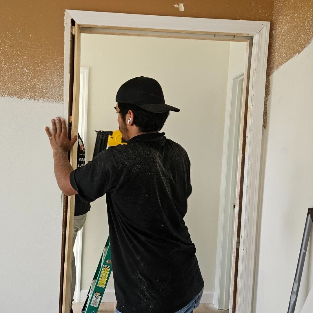 Carpenter repairing a termite-damaged door frame with new wood