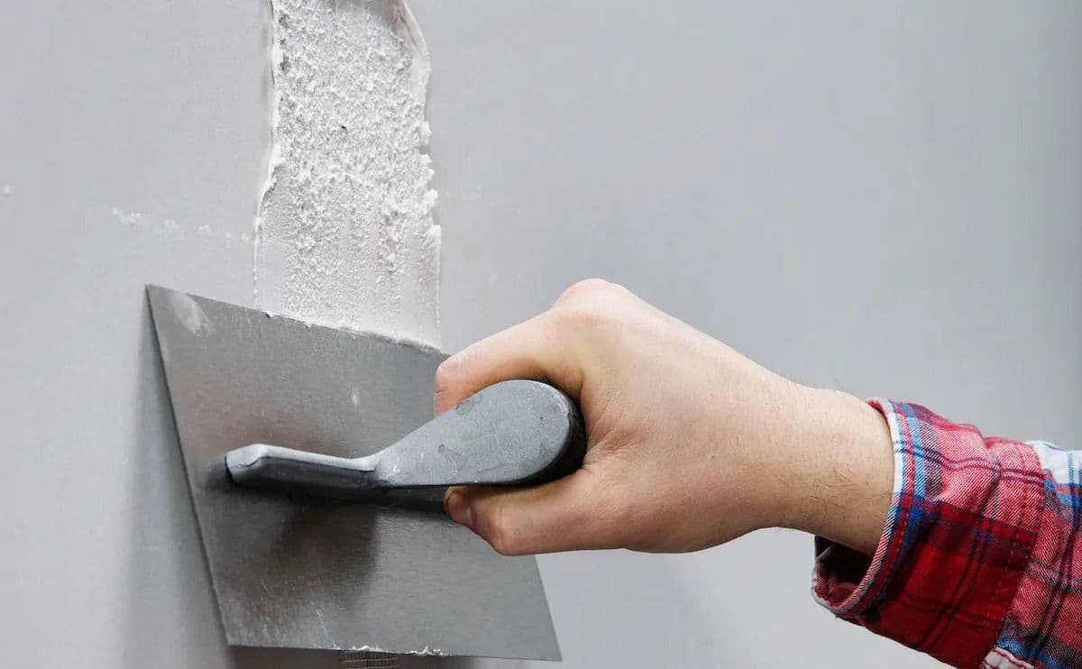 Plasterer skimming a wall after patching drill holes